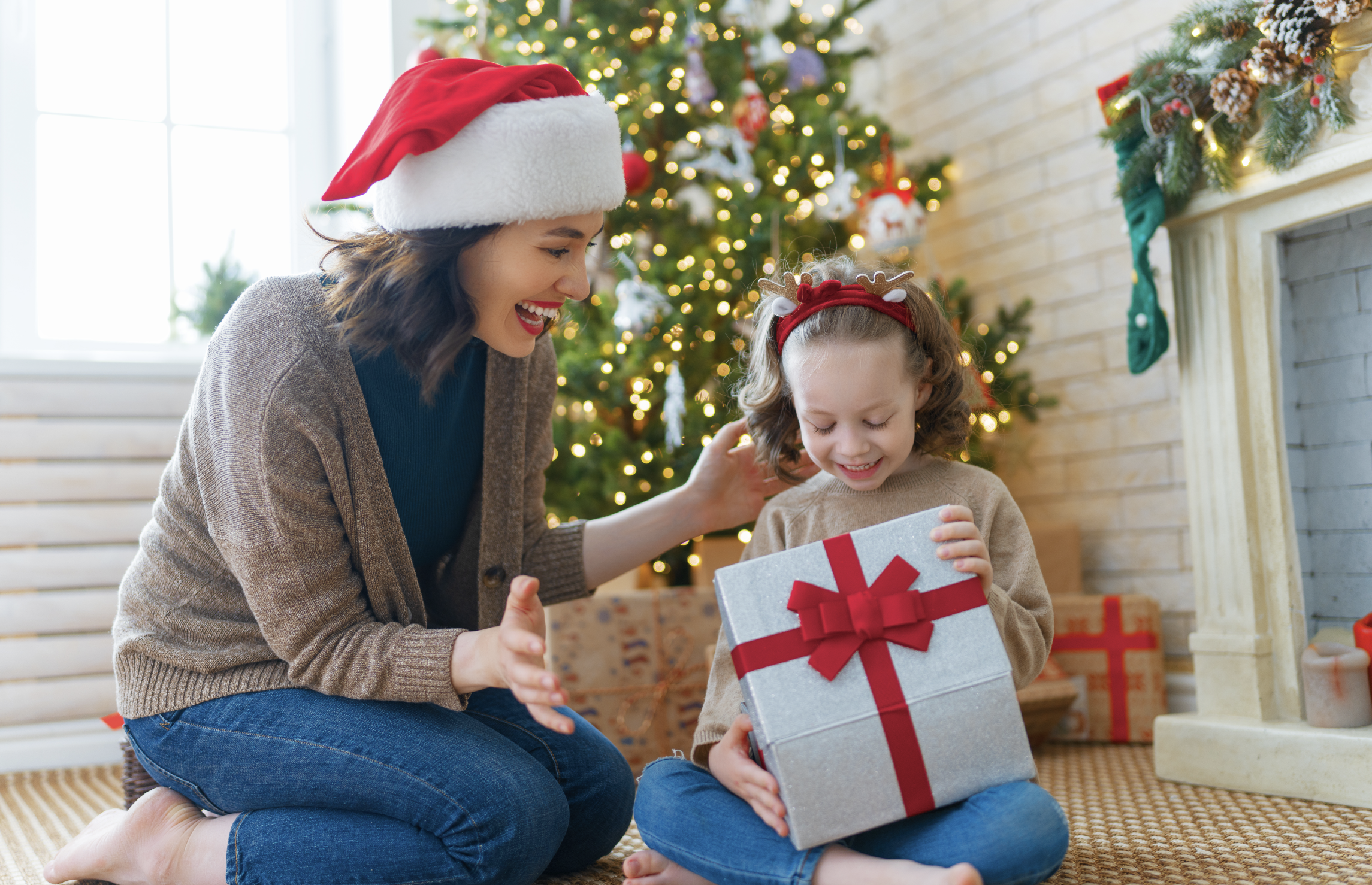 Woman and her daughter opening Christmas presents next to a live Christmas Tree